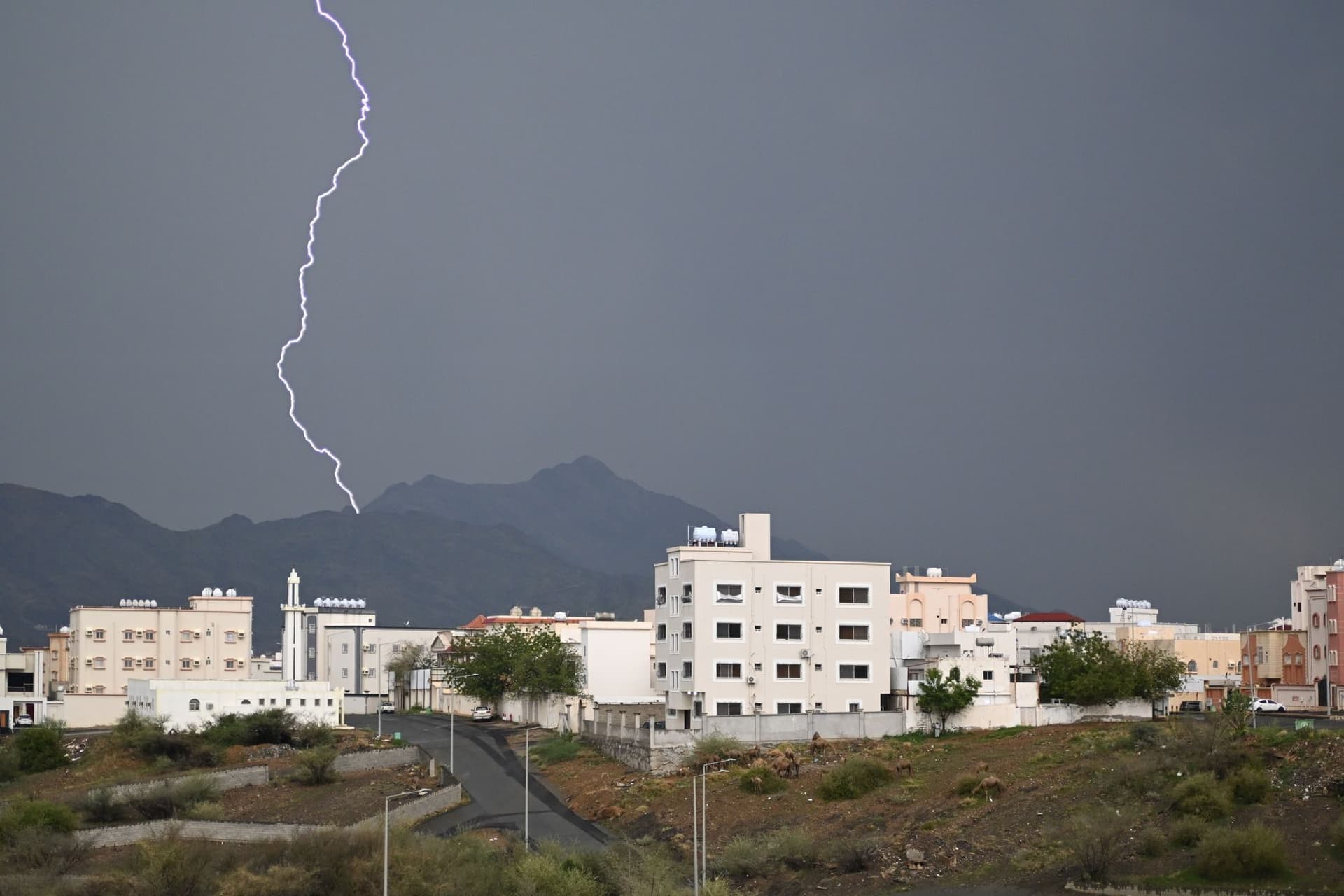 サウジアラビア南西部、アシール地方の市街と山並み。積乱雲から稲妻が落ちる。